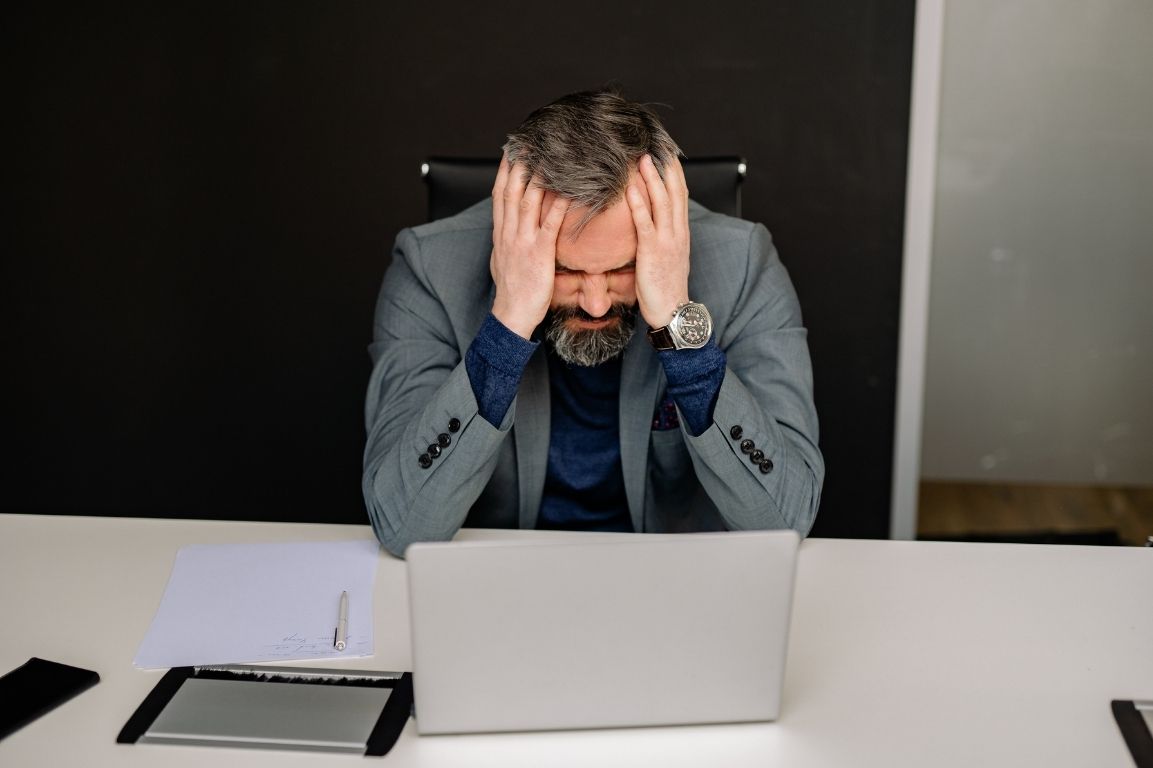 User-Inserted Stressed Business Leader Struggling With Leadership Challenges, Sitting At A Desk With Head In Hands, Symbolizing The Pressure And Stress Of Addressing Leadership Weaknesses In The Workplace.